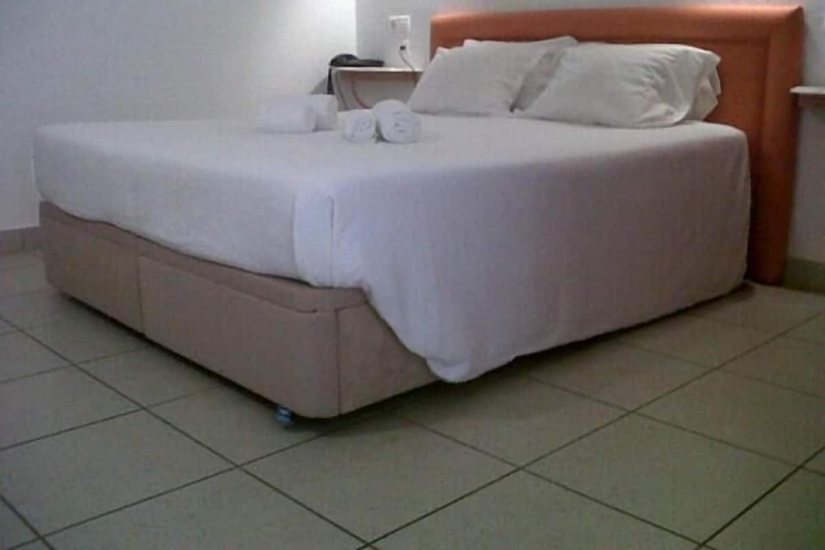 Un lit bien fait, avec une tête de lit, une table de chevet avec une lampe et une prise électrique au mur.