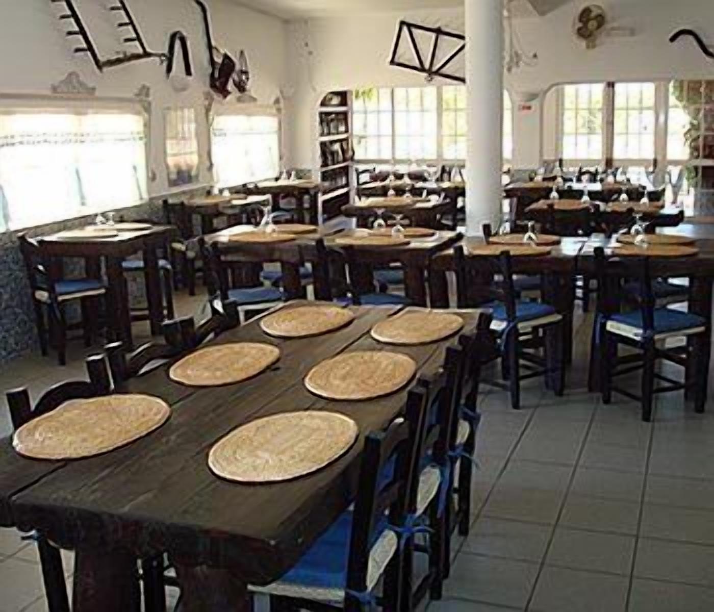 Een restaurant met meerdere tafels en stoelen, ruim ingericht met hoge plafonds en grote ramen voor natuurlijk licht.