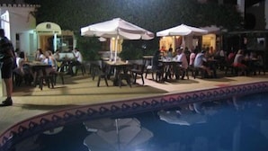 An outdoor dining area with tables and chairs, umbrellas, and a pool in the foreground. - Torre Velha (Albufeira)