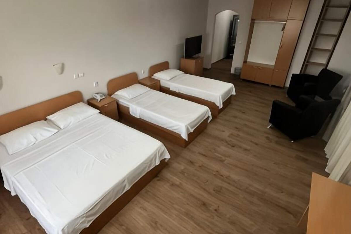 A hotel room with three beds, a desk, a chair, and a wardrobe.