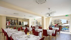 A restaurant with multiple tables, red chairs, and a bar area. - St Nicolas Elegant Residence (Paphos)