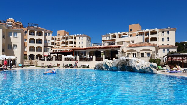 A swimming pool with clear blue water, surrounded by multi-story buildings with balconies and outdoor seating areas. - St Nicolas Elegant Residence (Paphos)