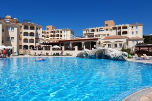 A swimming pool with clear blue water, surrounded by multi-story buildings with balconies and outdoor seating areas. - St Nicolas Elegant Residence (Paphos)
