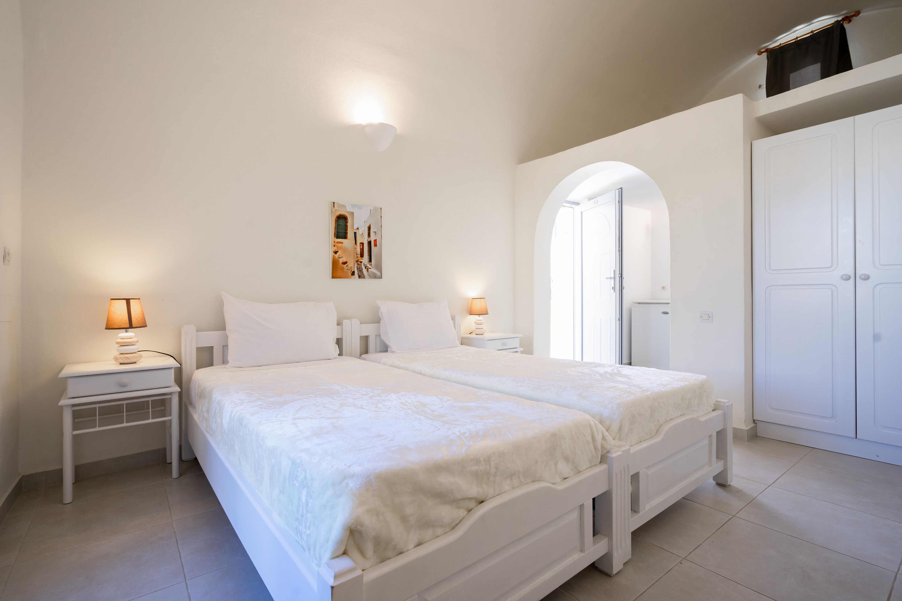 A bedroom with a double bed, two bedside tables with lamps, a wardrobe, and an arched doorway.