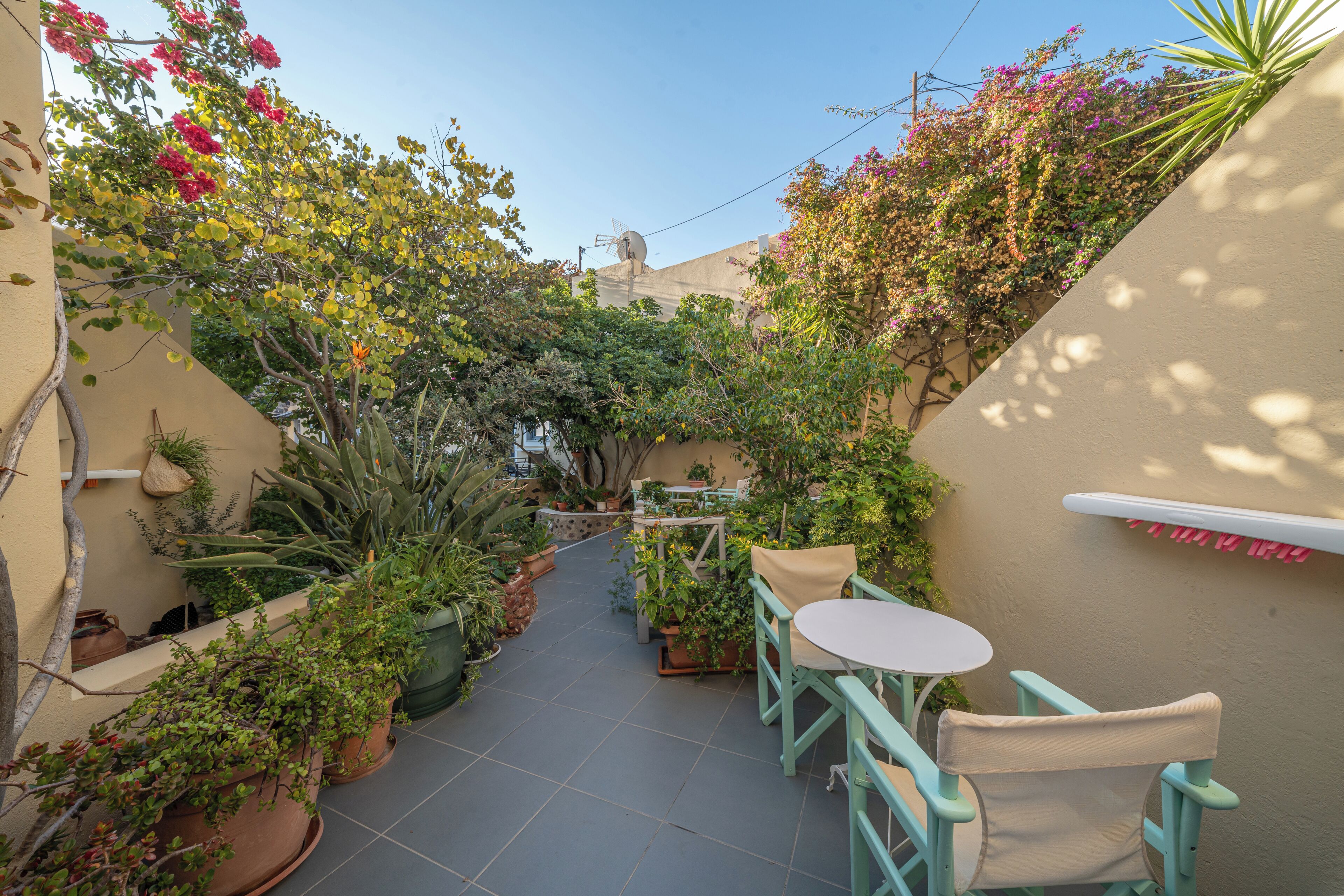 A narrow outdoor patio with potted plants, a table, and chairs.