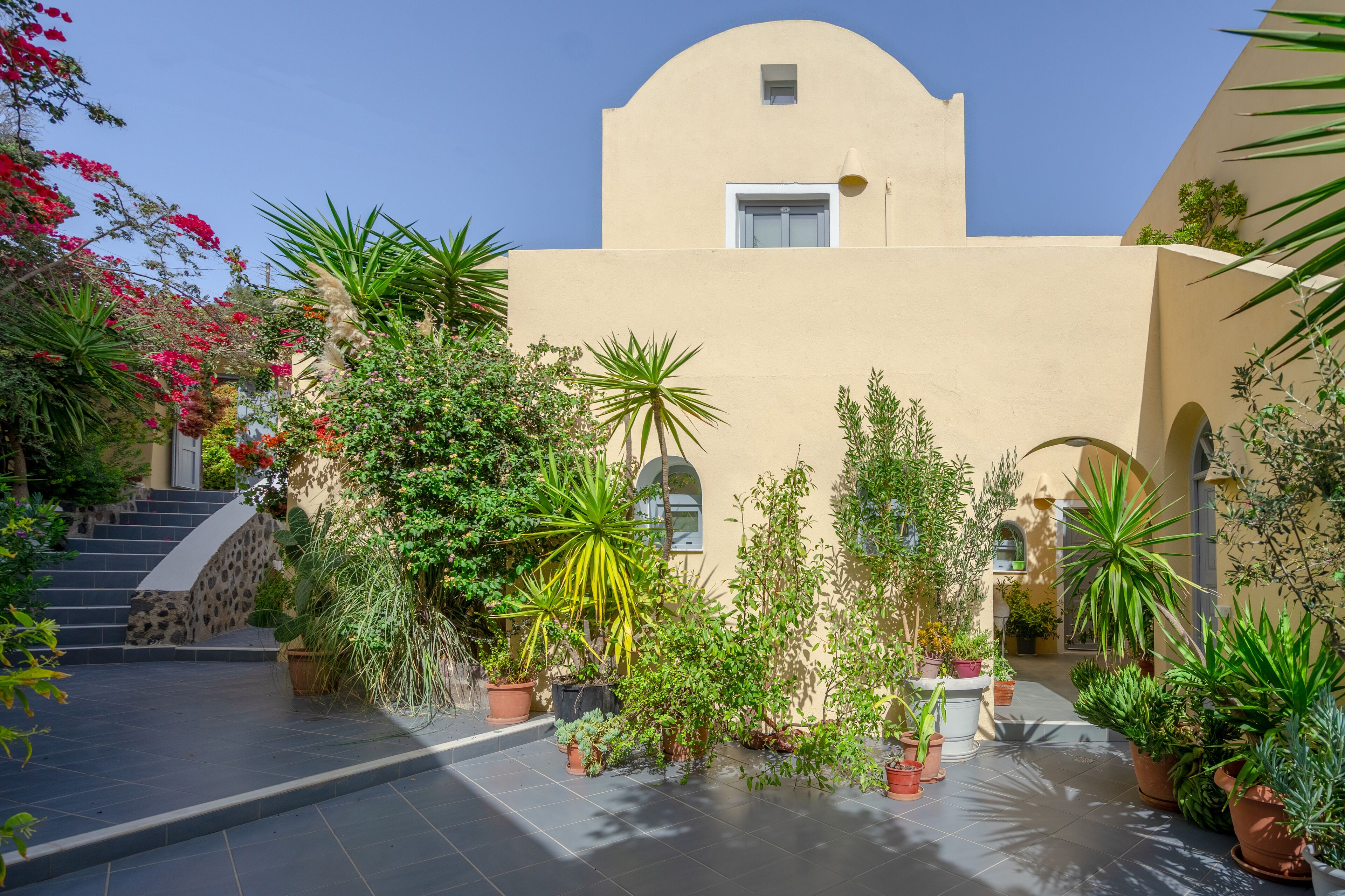 A courtyard with potted plants, a staircase, and a building with a curved facade.