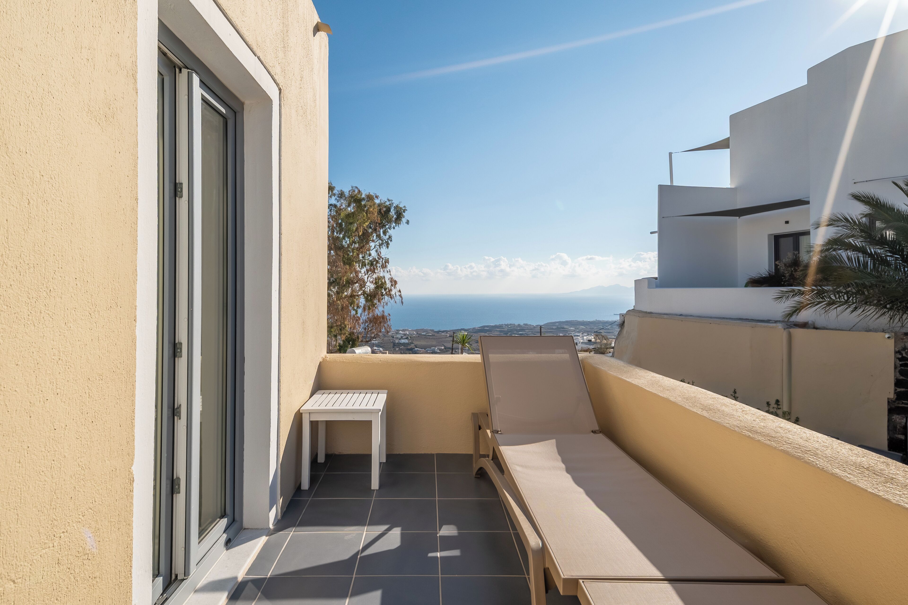 A balcony with a table and a chair, a view of the sea, and a building with a modern design.