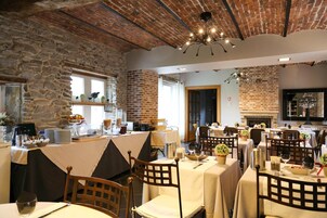 Un restaurante con paredes de ladrillo, vigas de madera y una chimenea. Las mesas están dispuestas con manteles blancos y sillas.