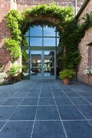 Un edificio de ladrillo con puerta de cristal, rodeado de vegetación y un patio con baldosas.
