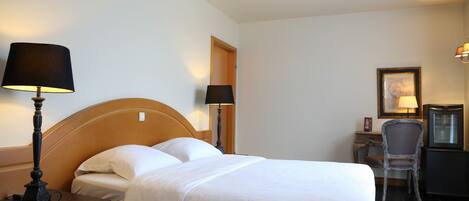 Una habitación de hotel con cama, lámparas de noche, escritorio, silla y televisión.