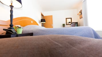 A hotel room with two beds, a bedside table with a lamp, a telephone, and a small potted plant.