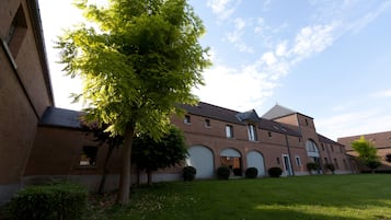 Un bâtiment en briques avec des fenêtres en arc de cercle et un grand arbre au premier plan.