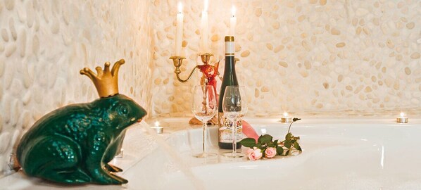Una bañera con una rana decorativa, una botella de vino y velas.