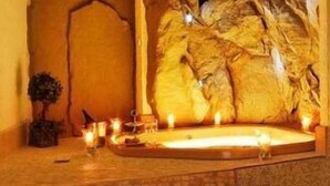 Een kamer met stenen vloer, een ruime, verlichte hottub en kaarsen.