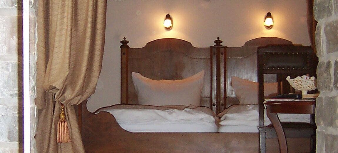 Un lit avec une tête de lit en bois, deux lampes fixées au mur et une table de chevet avec une lampe.