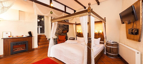 A four-poster bed with a stone wall backdrop, a fireplace, and a television mounted on the wall. - Märchenhotel (Bernkastel-Kues)