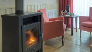 A cozy room with a wood-burning stove, two red armchairs, a small table with a decorative item, and a radiator.