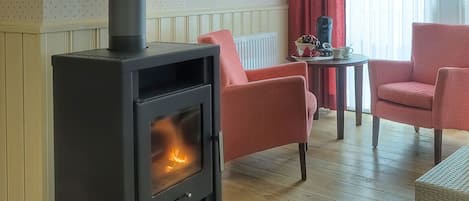 Una habitación acogedora con estufa de leña, dos sillones rojos, una mesita con un adorno y un radiador.