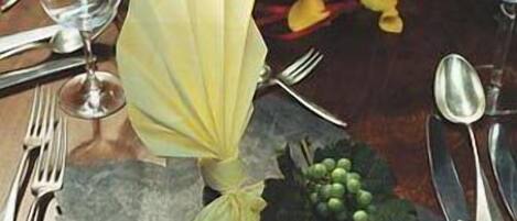 Una mesa dispuesta con una servilleta doblada, un pequeño ramo de uvas verdes y una hoja decorativa.