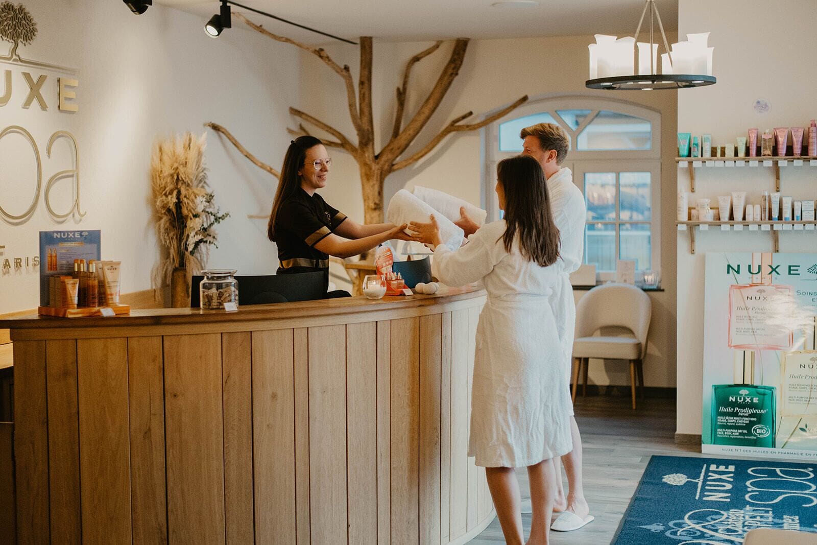 A reception area with a wooden counter, a large tree branch decoration, and a Nuxe product display.