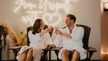 Una pareja con batas blancas sentada en una cama en una habitación con un letrero de neón que dice 'From Respect with a heart'.