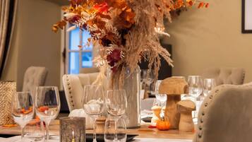 Una mesa de comedor dispuesta con copas de vino, una vela y un centro de mesa con flores secas y follaje.