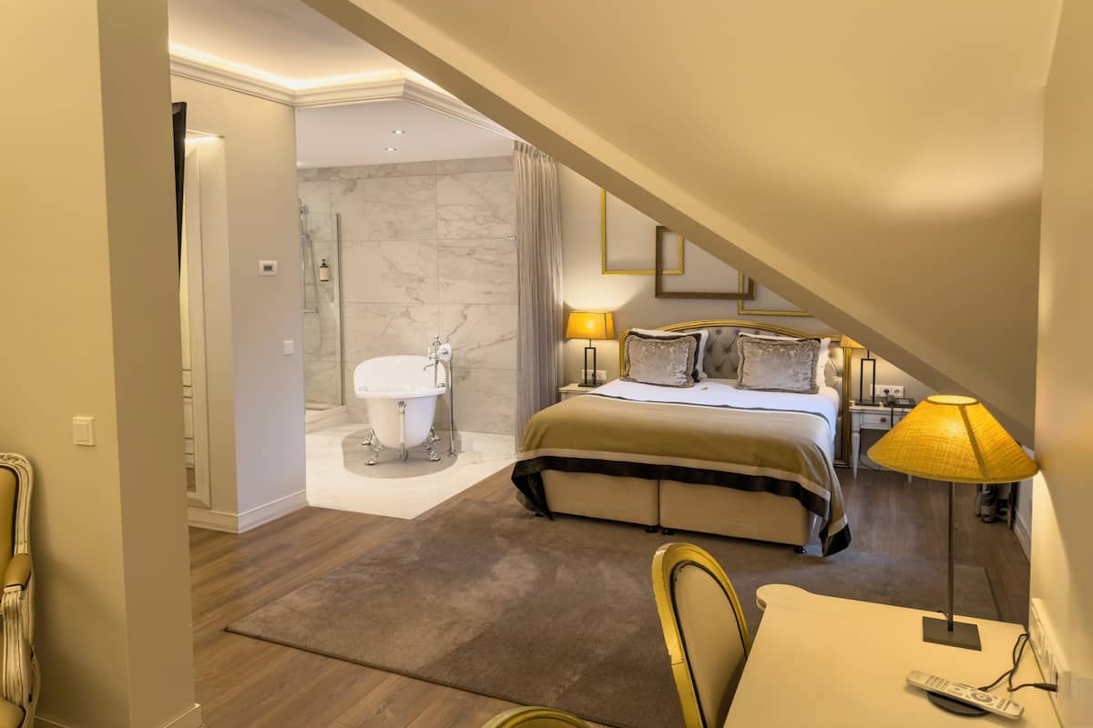 A hotel room with a bed, bedside table, lamp, and a bathroom with a bathtub and shower.