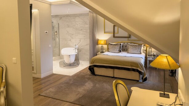 Une chambre d’hôtel comprenant un lit, une table de chevet, une lampe, ainsi qu’une salle de bain avec une baignoire et une douche.