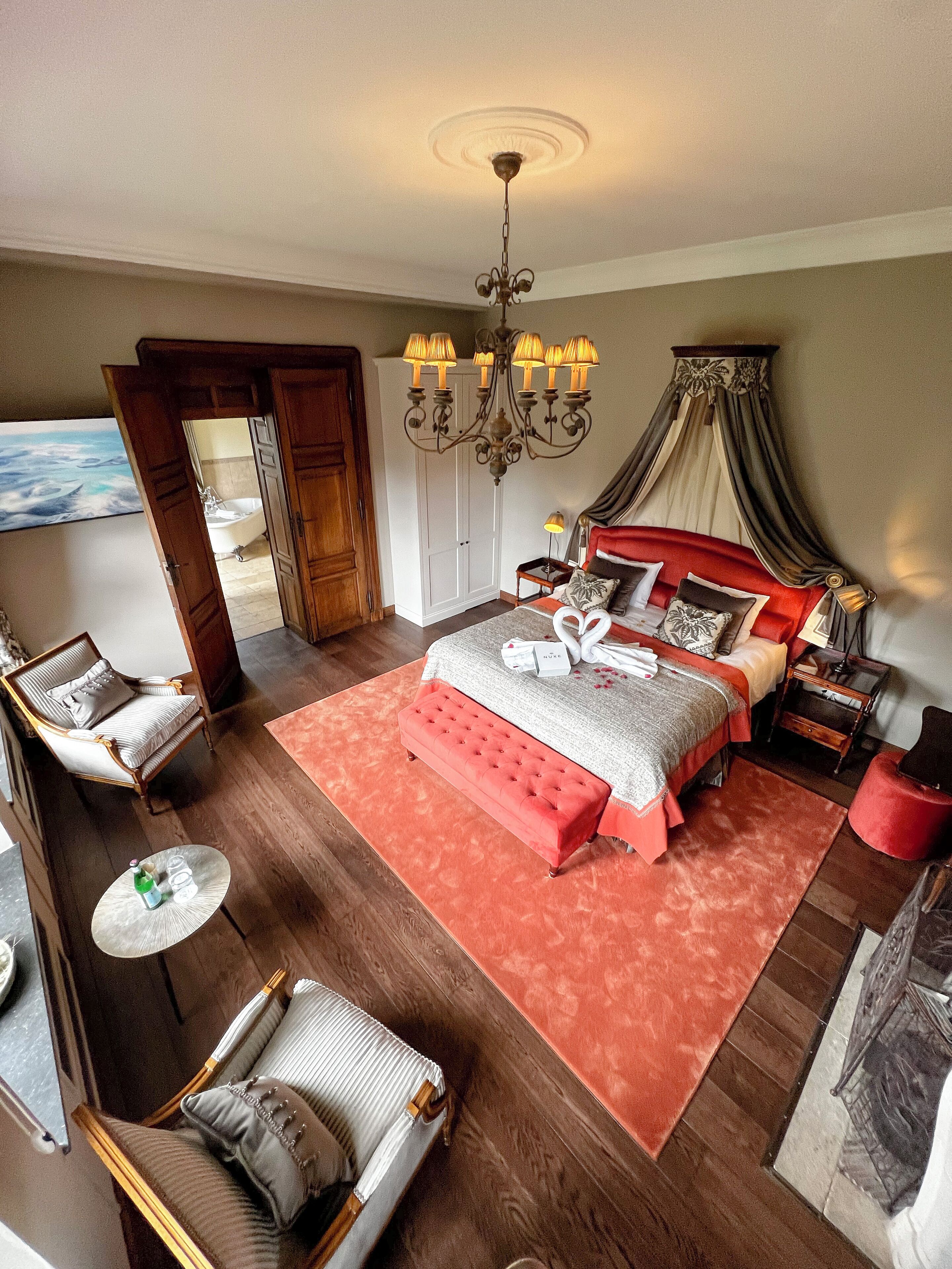 Een ruime slaapkamer met een groot bed, een kroonluchter en uitzicht op de badkamer.