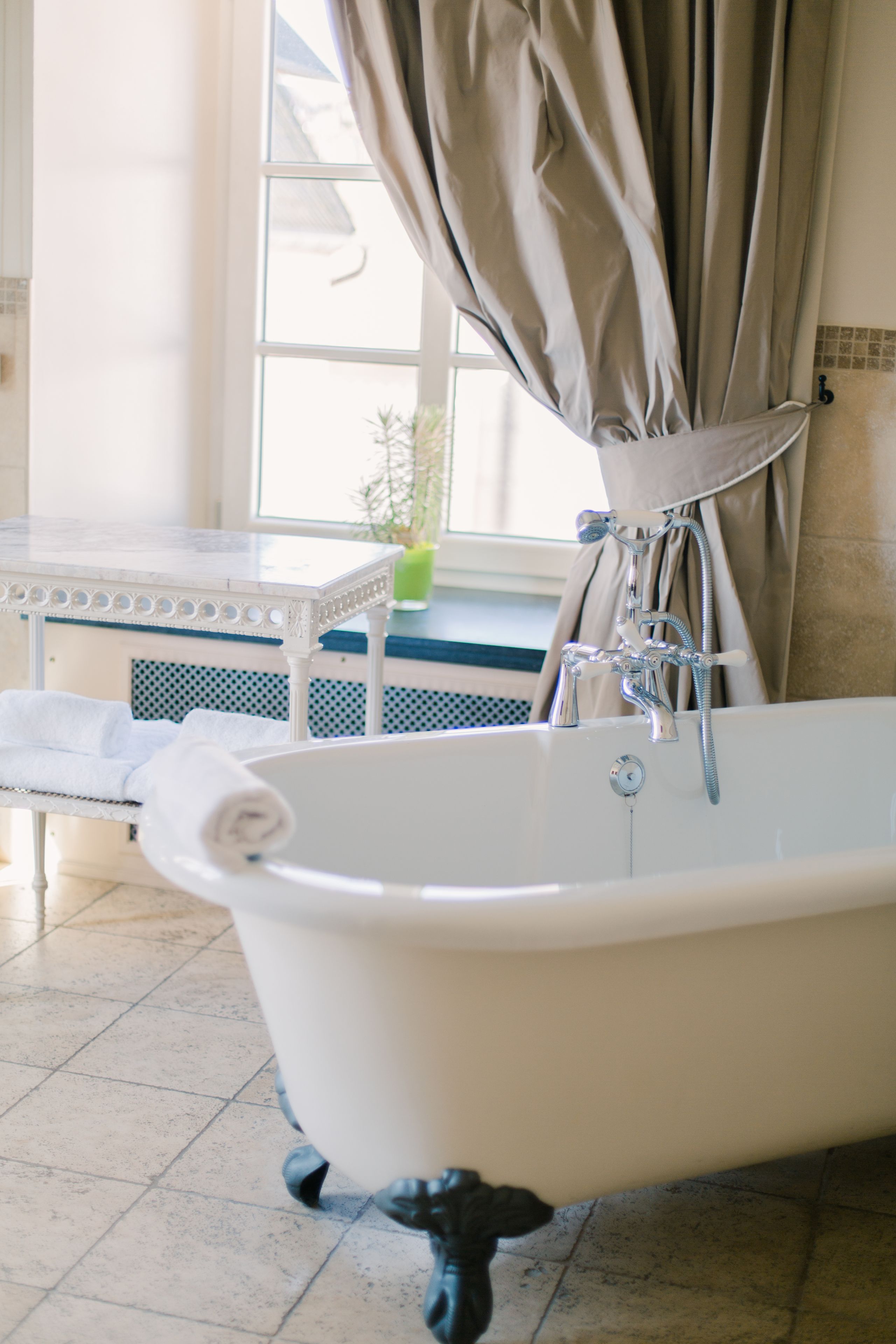 Un bagno con una vasca da bagno a piedi di leone, una finestra con tende e un piccolo tavolino con un asciugamano.
