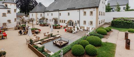 Un patio con mesas al aire libre, un brasero y arbustos bien cuidados.
