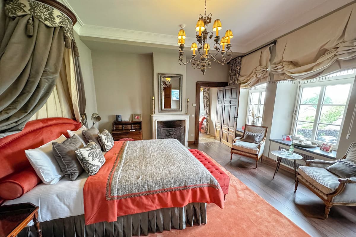 A spacious bedroom with a large bed, a fireplace, a chandelier, and a view of the outdoors.