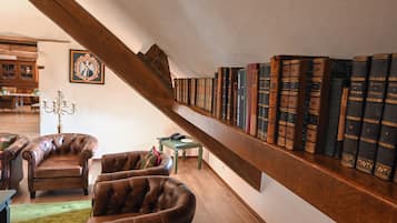 Une bibliothèque dotée de fauteuils en cuir, d’un escalier en bois et d’une collection de livres rangés sur des étagères.