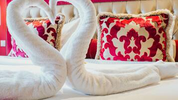 A bed with white towels arranged in a heart shape, red and white patterned pillows, and a tufted headboard.