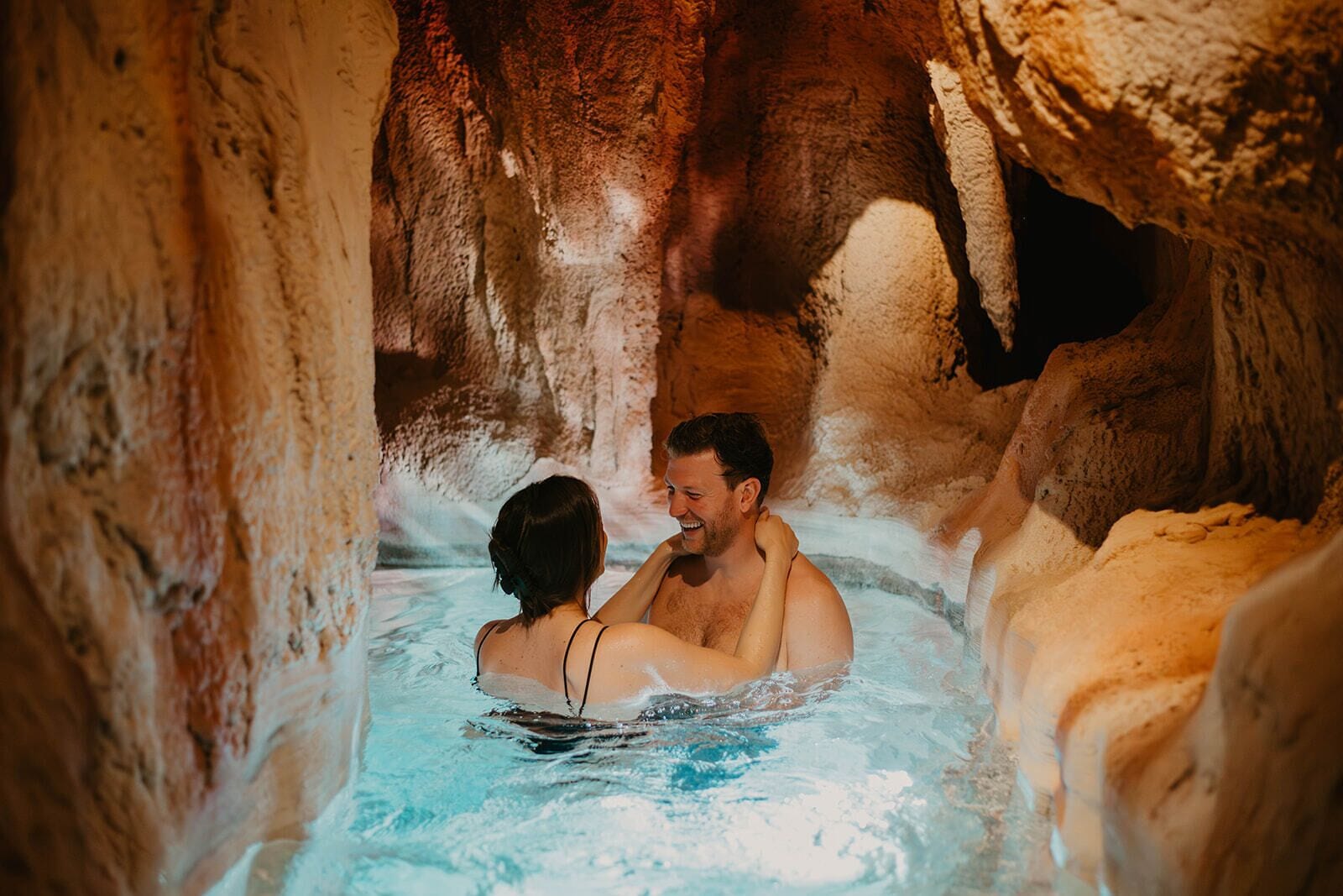 A couple in a hot spring with natural rock formations around them.