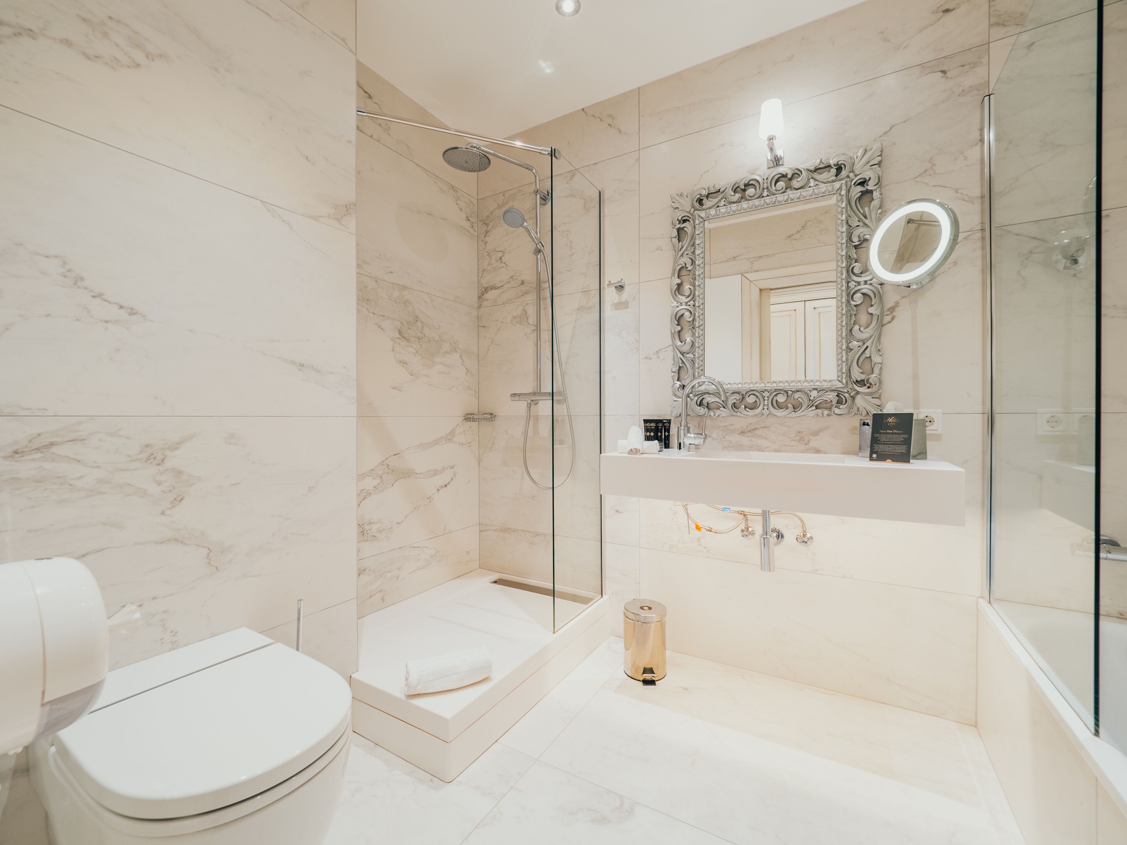 Une salle de bain moderne dotée d’une douche à parois de verre, d’un sol carrelé en marbre, de toilettes blanches et d’un meuble-lavabo avec un miroir.