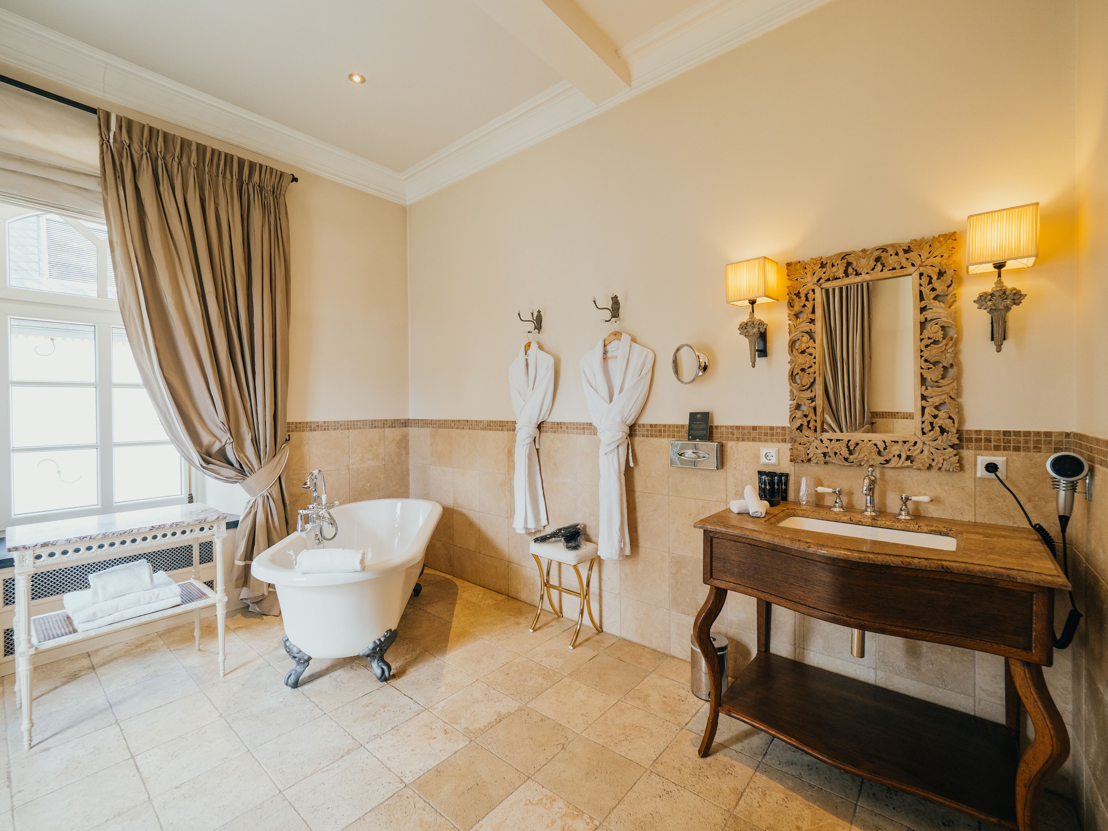 A bathroom with a freestanding bathtub, a vanity with a mirror, and two towels hanging on hooks.