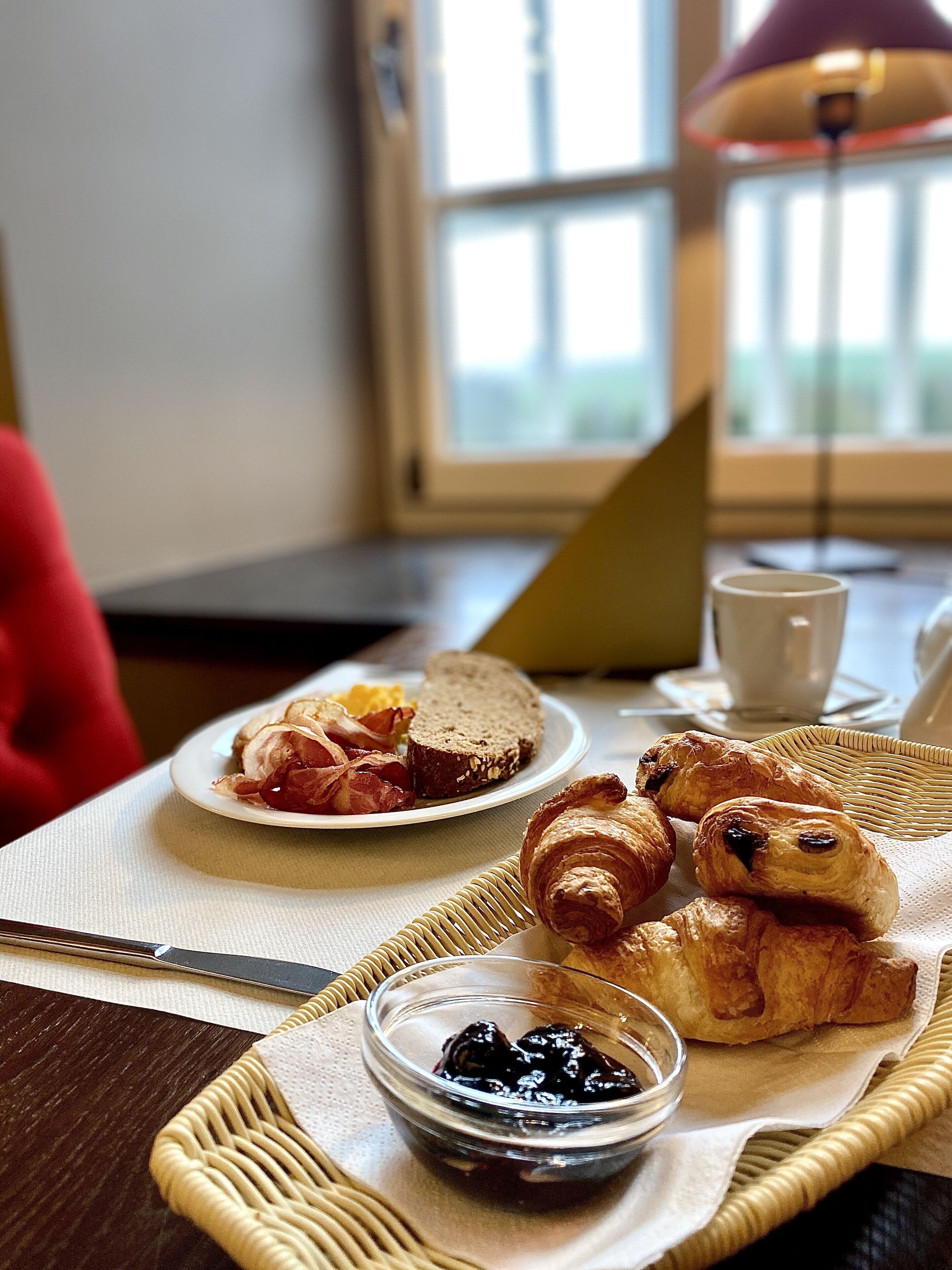 A breakfast setting with croissants, a plate of bacon and eggs, and a bowl of jam on a table.