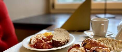 A breakfast setting with croissants, a plate of bacon and eggs, and a bowl of jam on a table.