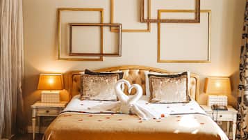 Una cama grande con cabecera dorada, dos mesitas de noche con lámparas, y una pared decorada con diseños geométricos enmarcados.