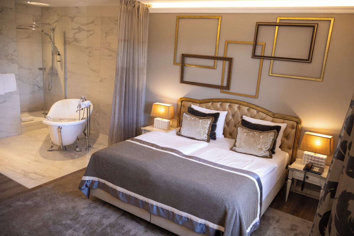 A bedroom with a large bed, a bathtub, and a shower.