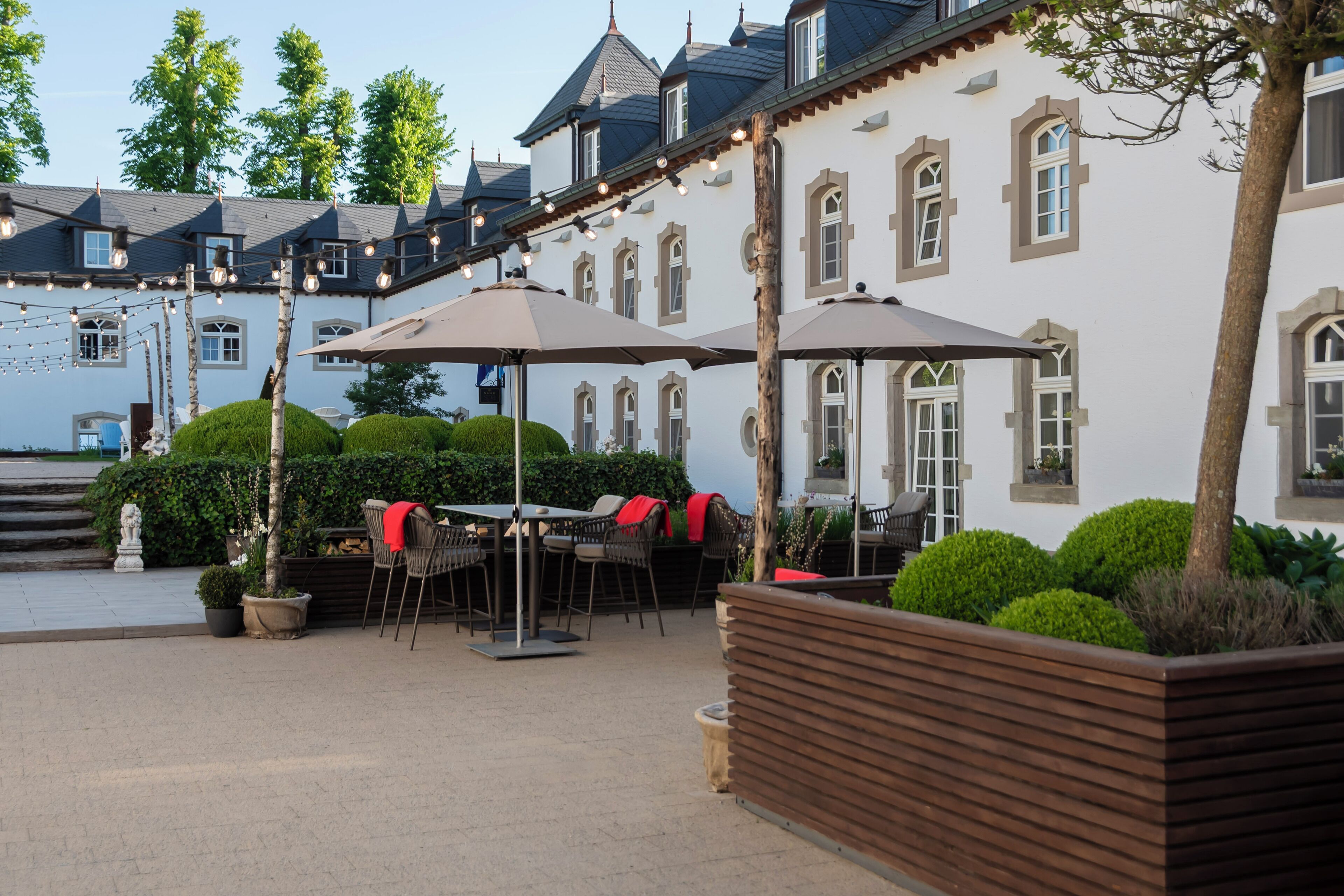A courtyard with outdoor seating, a wooden planter, and a building with multiple windows and a balcony.