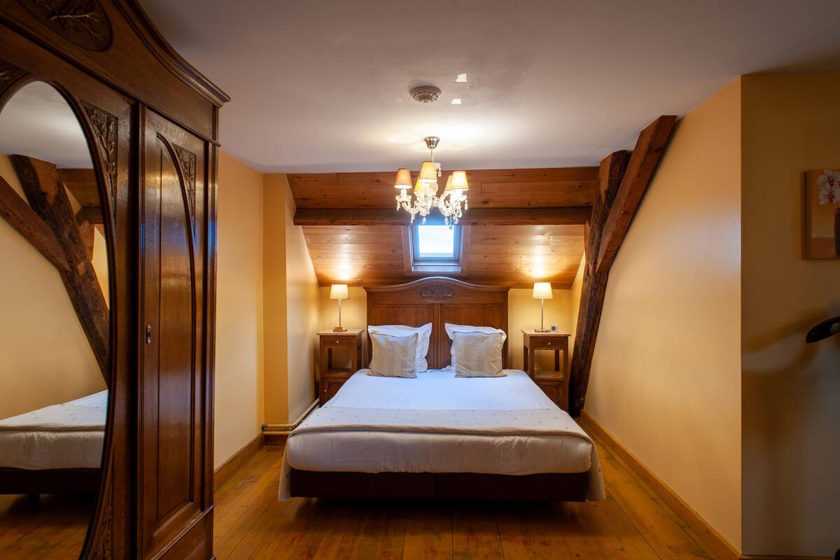 Une chambre avec un grand lit, des murs en bois, un lustre et une lucarne.