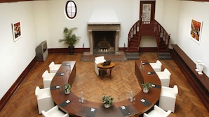 Un salón de conferencias con una gran mesa ovalada, sillas blancas, una chimenea, una escalera de madera y un tragaluz.
