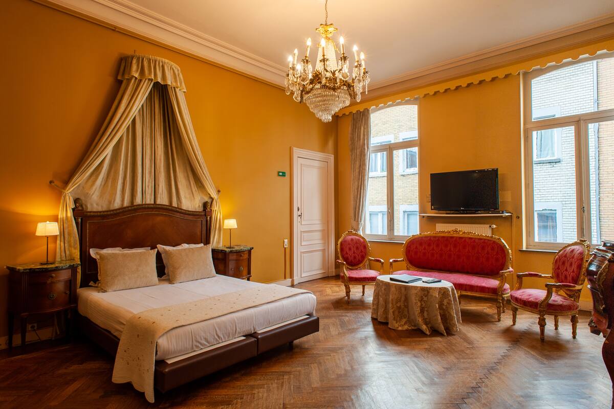 Une chambre d’hôtel avec un grand lit, un lustre, une télévision et un canapé rouge.