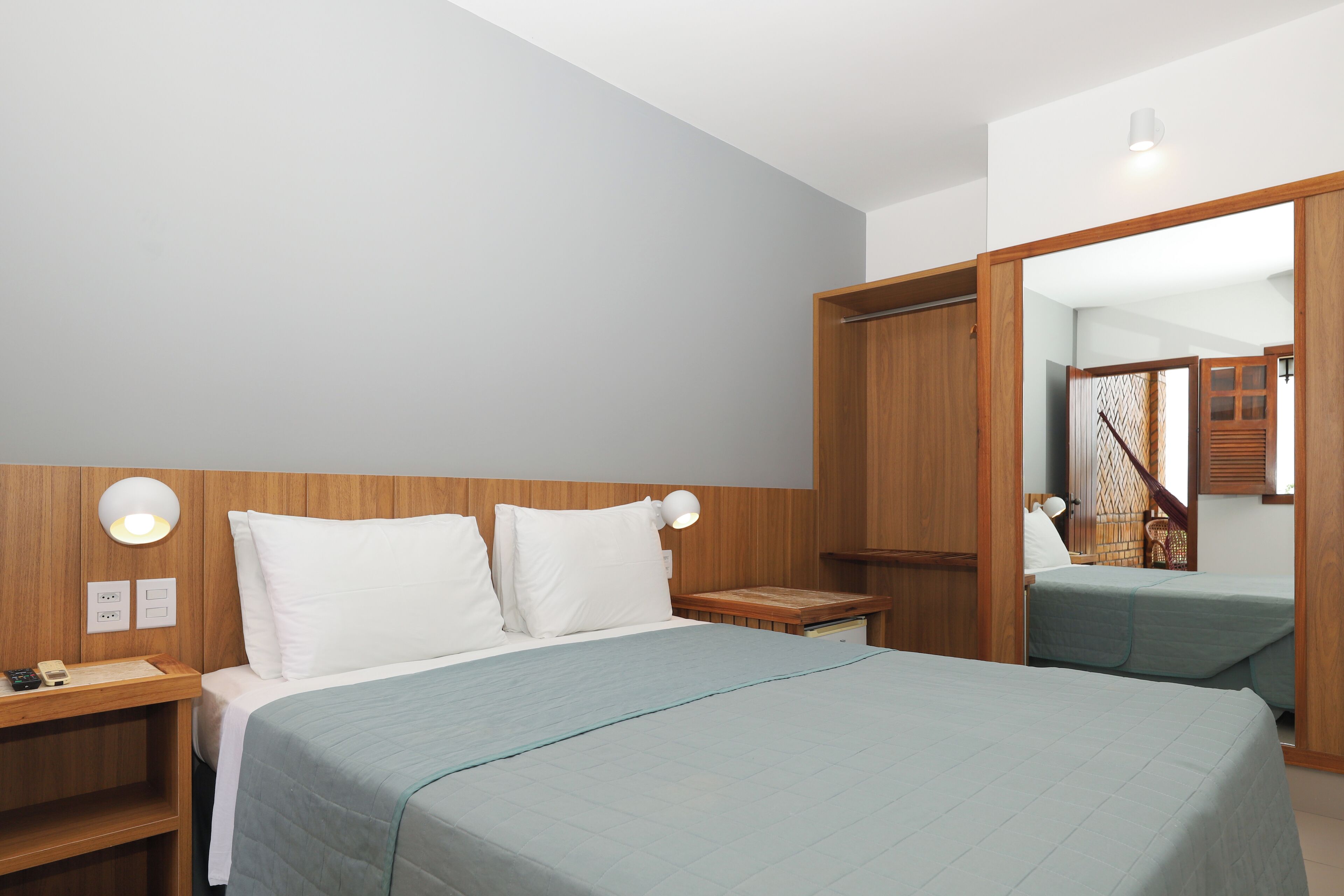 A hotel room with a bed, bedside tables, a mirror, and a wardrobe.