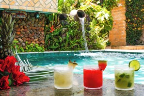 A poolside setting with a stone wall, a water feature, and three drinks with garnishes. - Pousada da Ladeira (Tibau do Sul)
