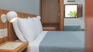Habitación de hotel con cama, lámpara de noche, cabecero de madera, ventana con persianas y equipo de aire acondicionado.