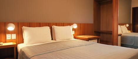 A hotel room with a large bed, two bedside tables, a nightstand, a wooden wardrobe, and a mirror.