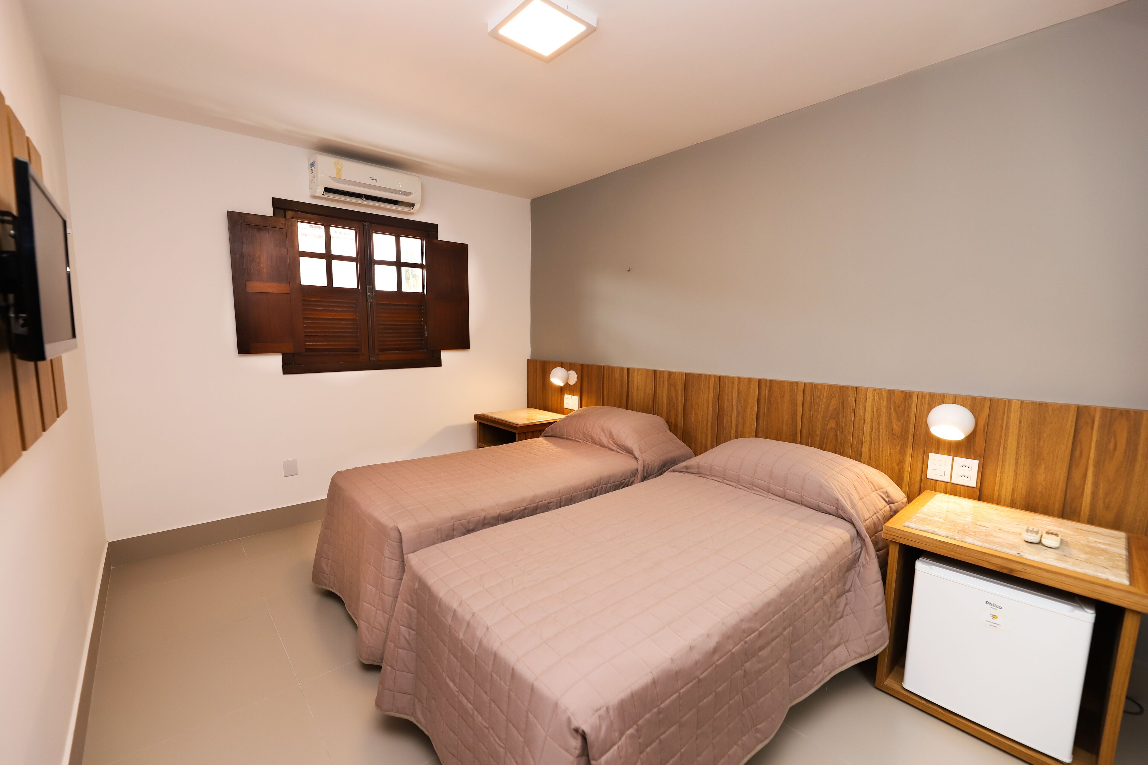 A bedroom with two beds, a small wooden nightstand, a wall-mounted air conditioner, and a television.